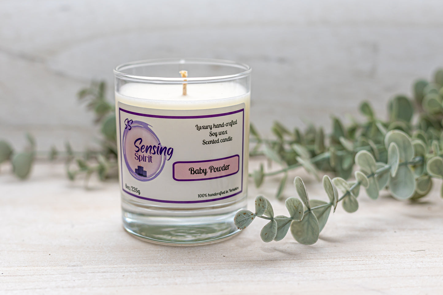 Baby powder scented soy wax candle surrounded by green leaves