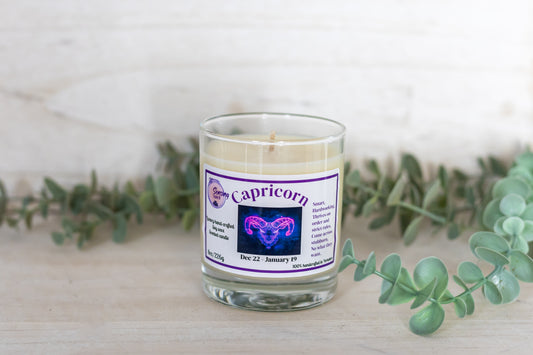 Candle with a Capricorn label on a white surface with greenery