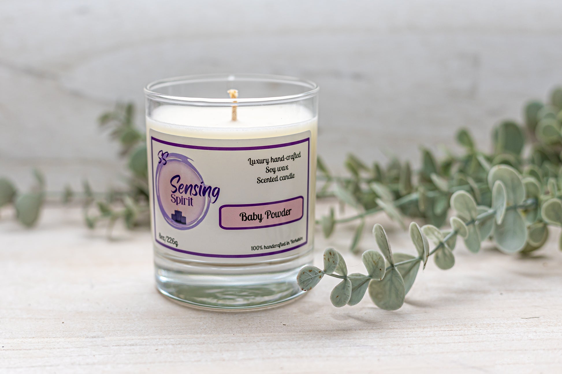 Baby powder scented soy wax candle surrounded by green leaves