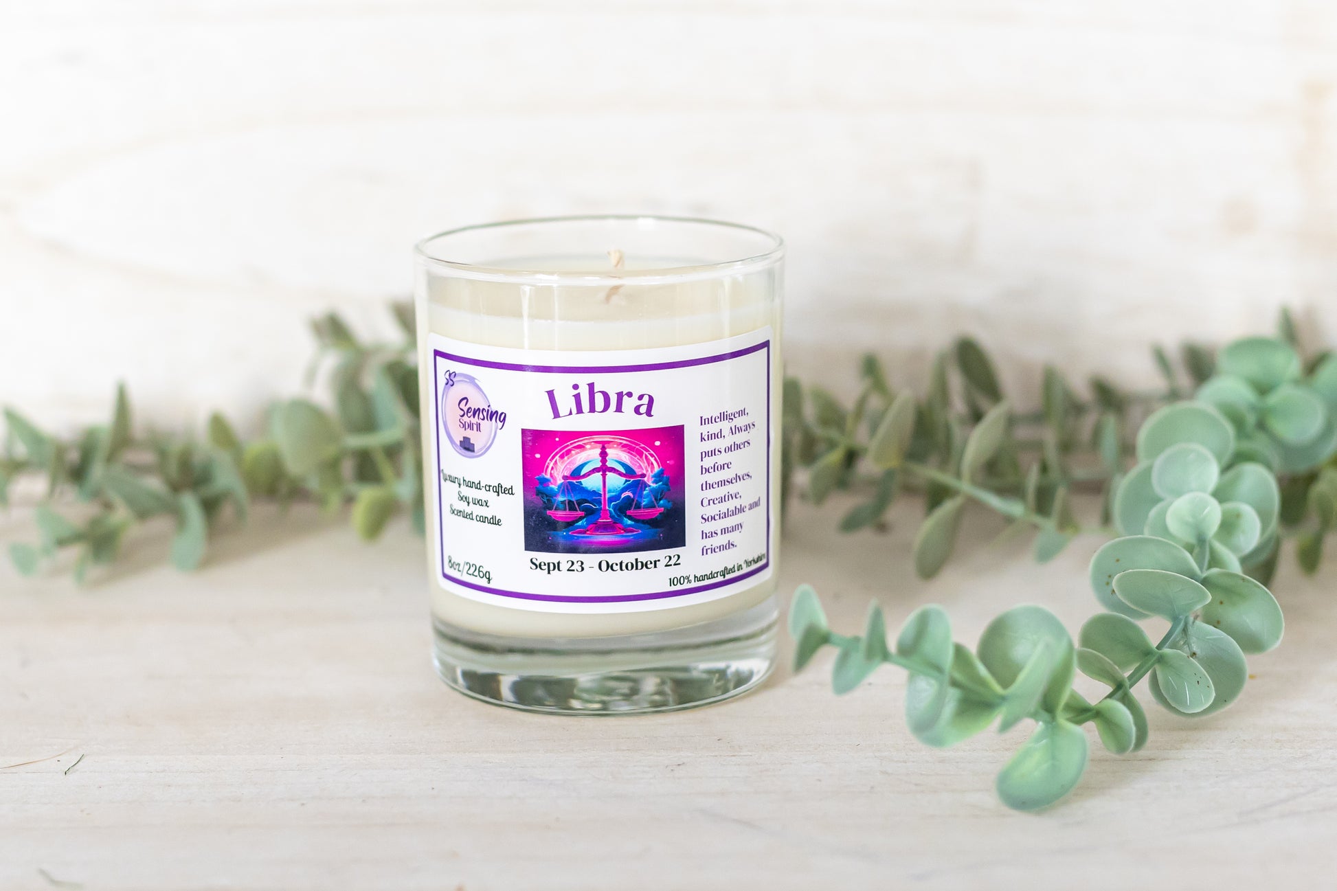 Candle labeled 'Libra' with eucalyptus leaves on a light background