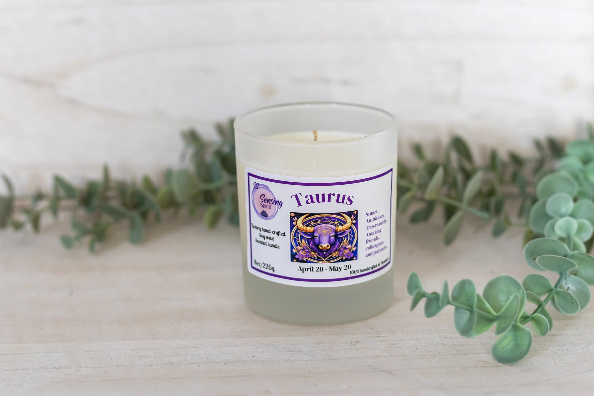 Candle with Taurus label on a white surface with greenery